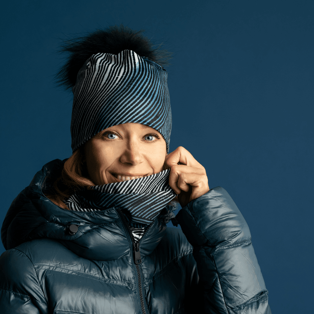 Femme portant une veste d'hiver foncée, souriant et ajustant une tuque et un cache-cou assortis à motif abstrait.