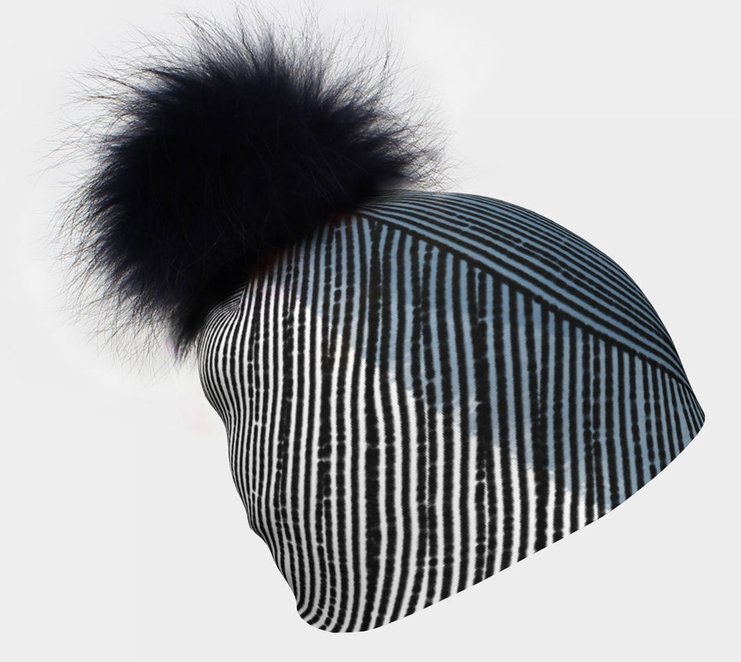 Gros plan d'une tuque avec des rayures verticales abstraites bleues, blanches et noires, surmontée d'un grand pompon noir.