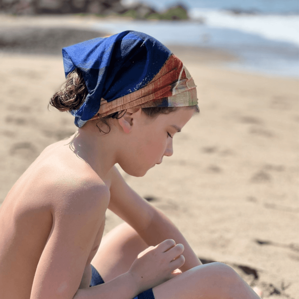 Un enfant sur la plage porte le tube de cou à motif abstrait jaune et bleu comme bandana.