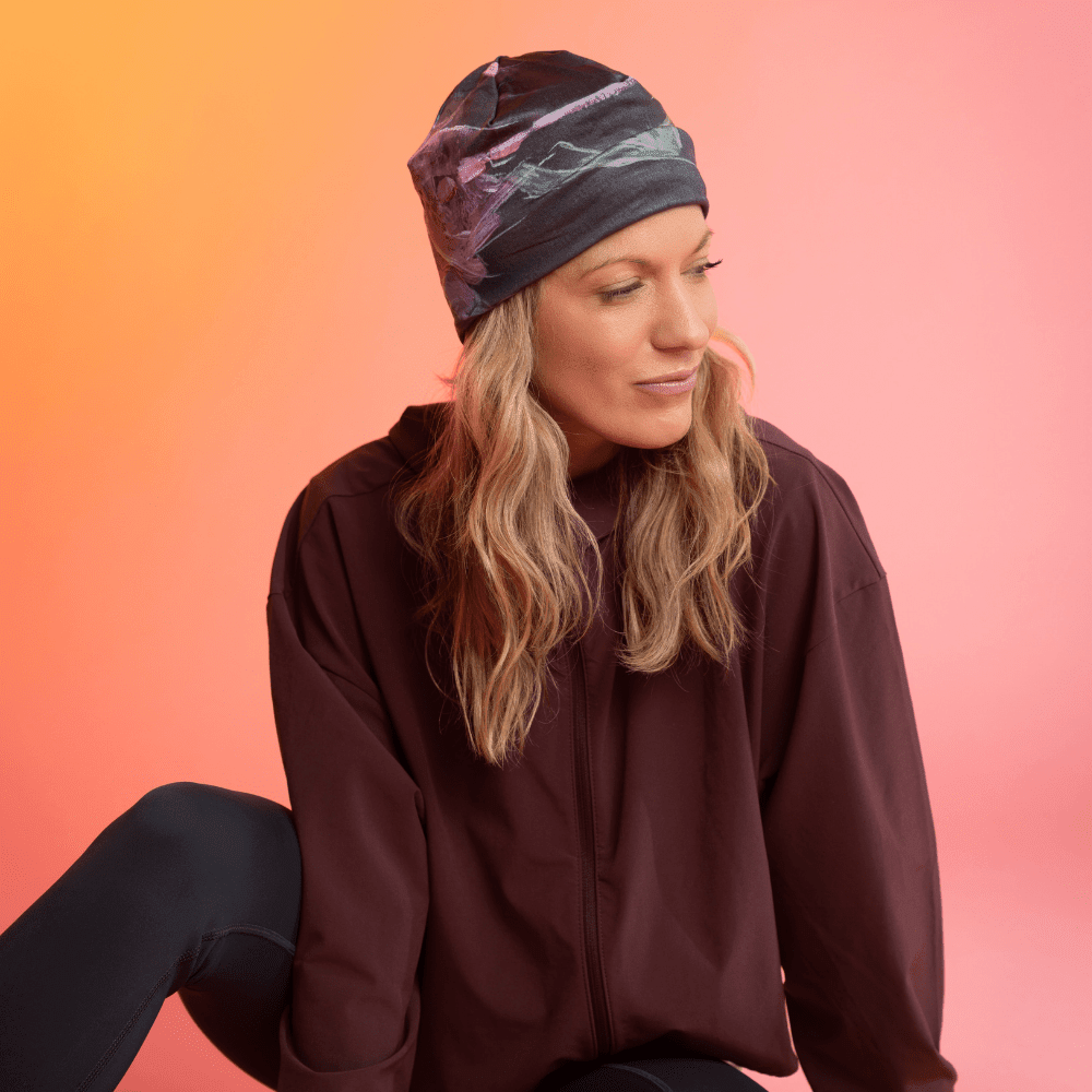 Une femme portant une tuque noire avec un imprimé floral abstrait rose et vert regarde pensivement sur le côté.