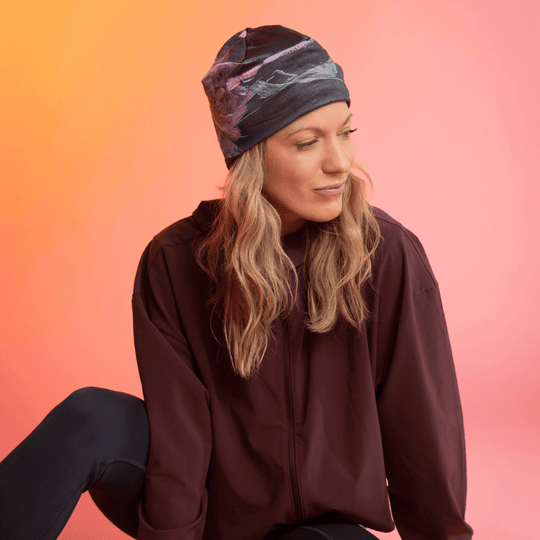 Une femme portant une tuque noire avec un imprimé floral abstrait rose et vert regarde pensivement sur le côté.