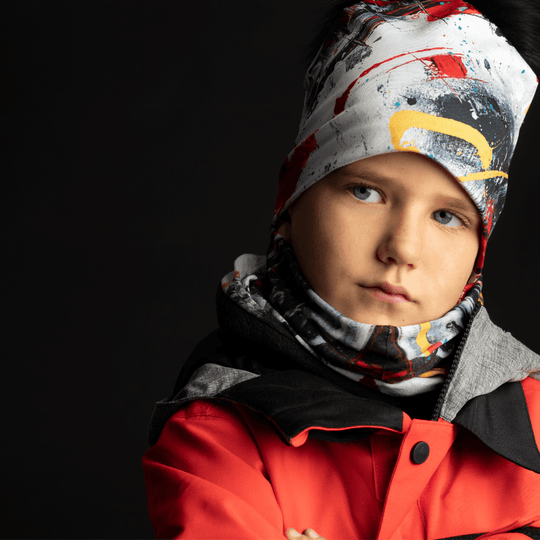Un jeune garçon portant une tuque abstraite colorée et un cache-cou, regardant sérieusement.