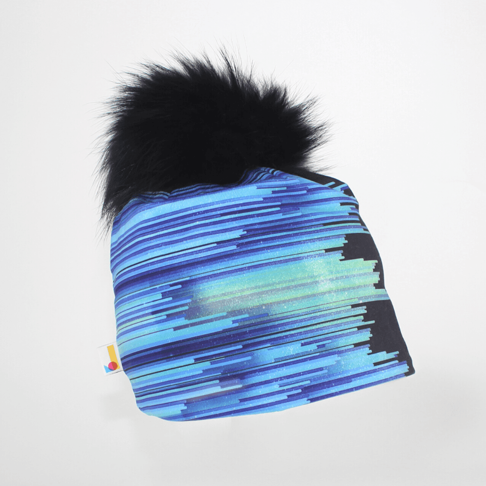 Tuque "Black War" à rayures abstraites bleues et violettes et gros pompon noir, sur fond blanc.