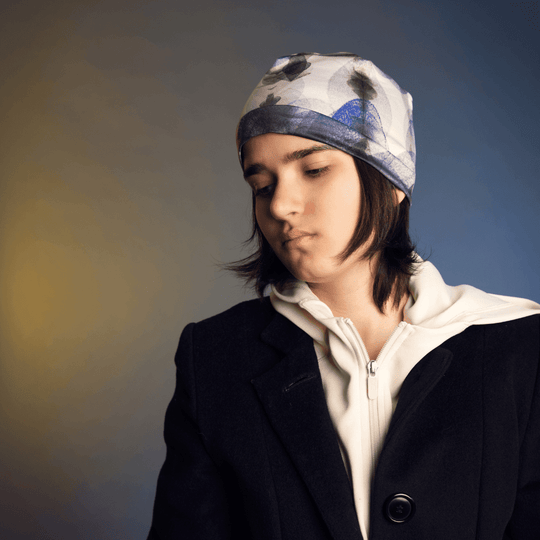 Side profile of a model wearing the Blue Feathers Beanie, looking down against a yellow and blue background.