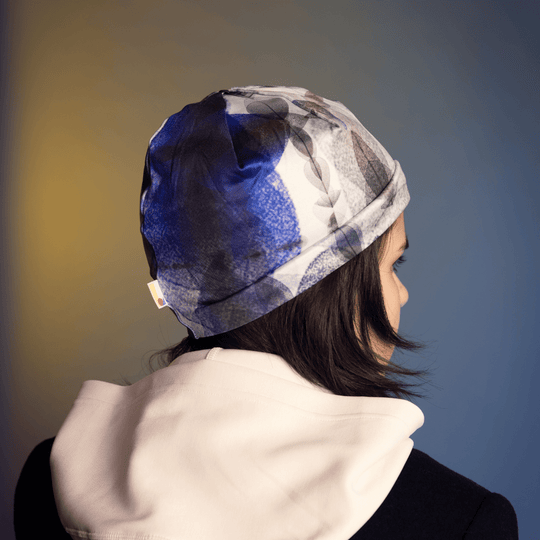 Back view of a model wearing the Blue Feathers Beanie, showing the artistic pattern against a blue background.