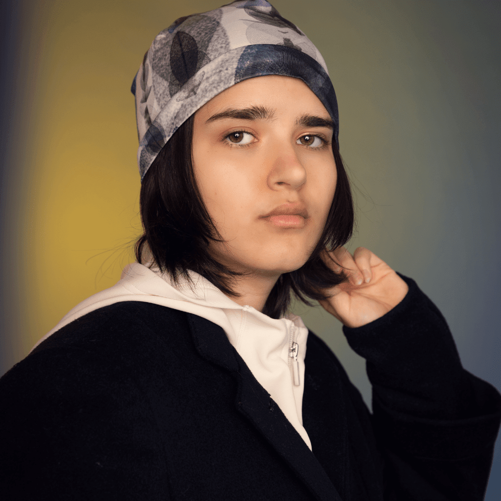 Model wears the Blue Feathers Beanie with a white hoodie and black jacket against a colourful backdrop.