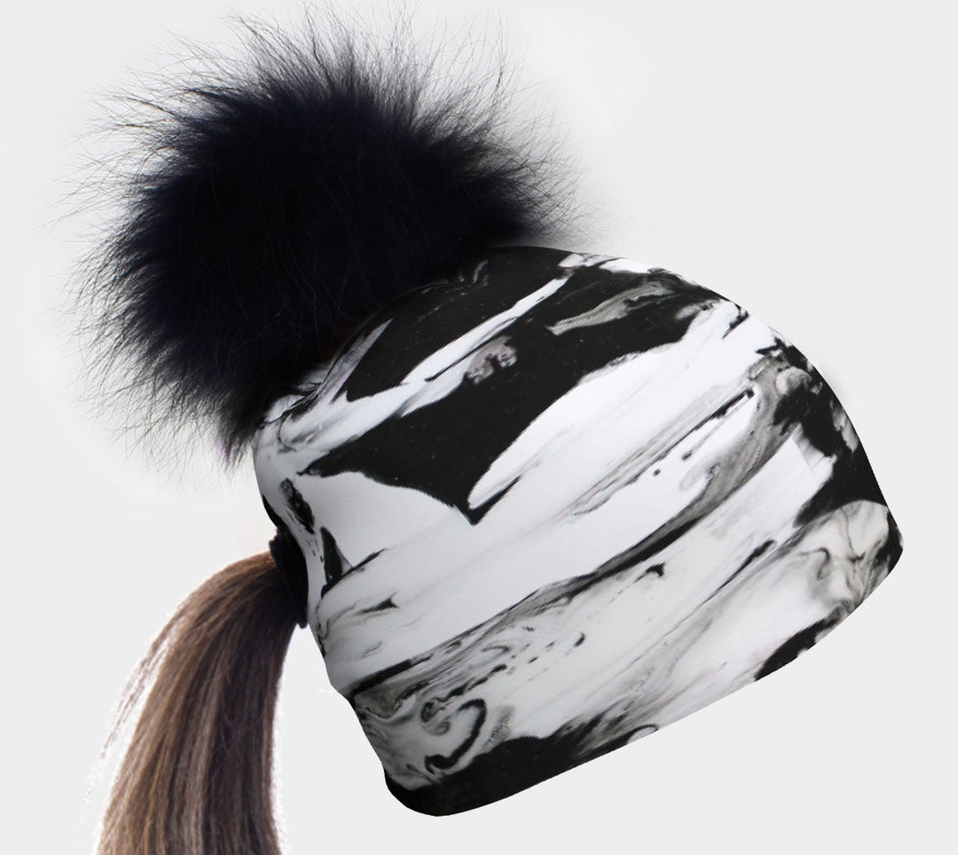 Tuque à motif marbré noir et blanc avec un gros pompon noir sur le dessus et une queue-de-cheval dépassant d'un trou à l'arrière.