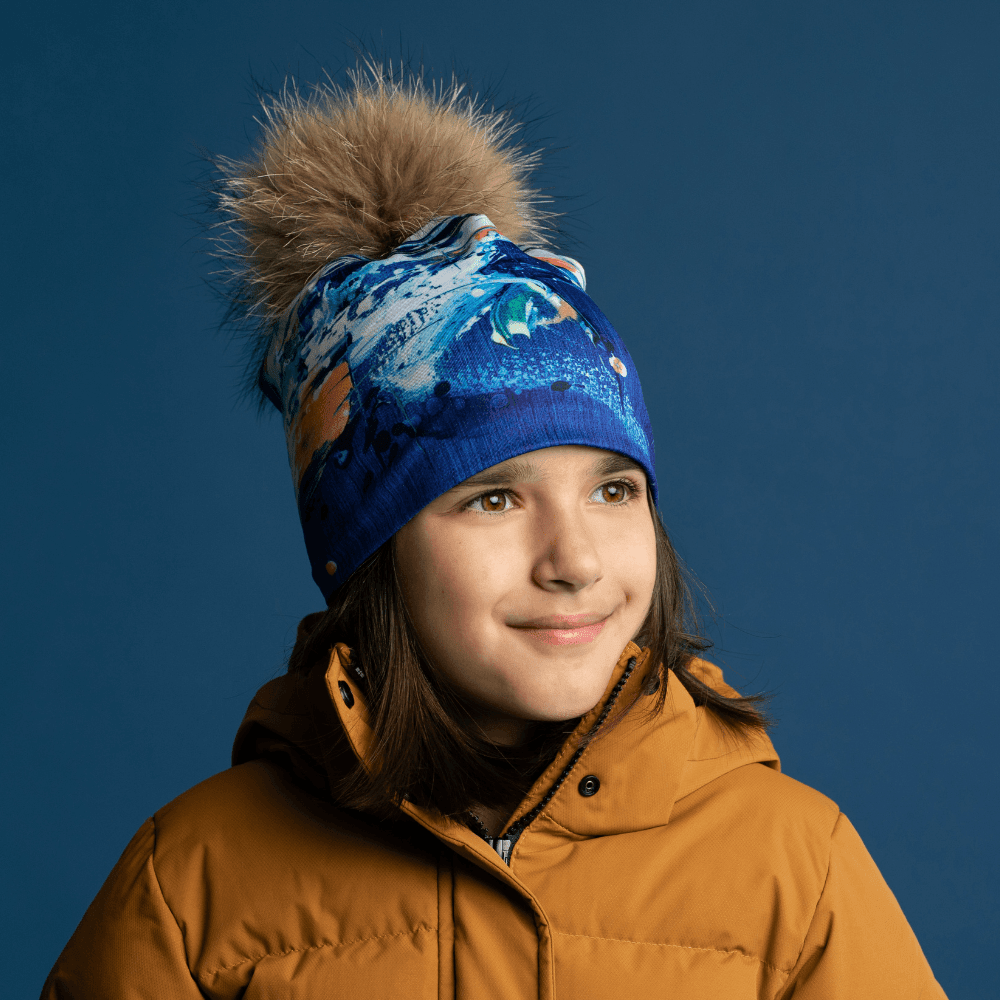 Jeune fille portant la tuque bleue aux couleurs d'art abstrait avec un pompon moelleux et une veste jaune.