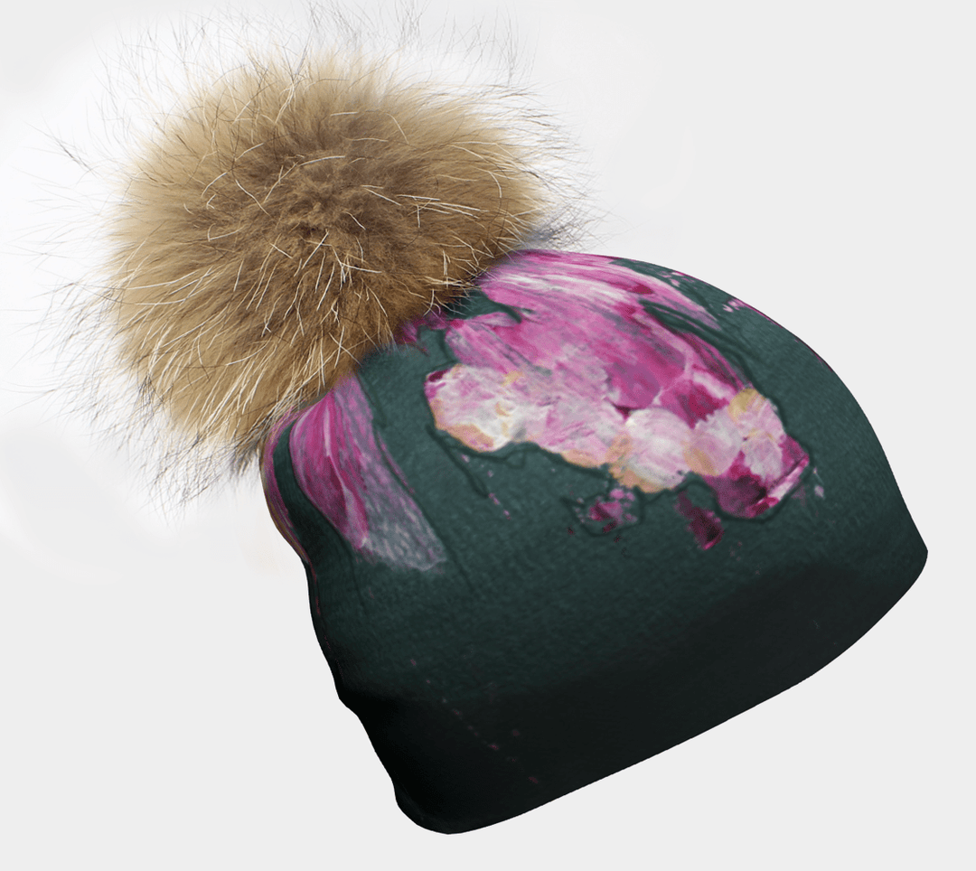 Gros plan de la Tuque Fleur Glitch, montrant sa base bleu sarcelle foncé avec des touches abstraites florales rose vif et blanches et un grand pompon brun moelleux.