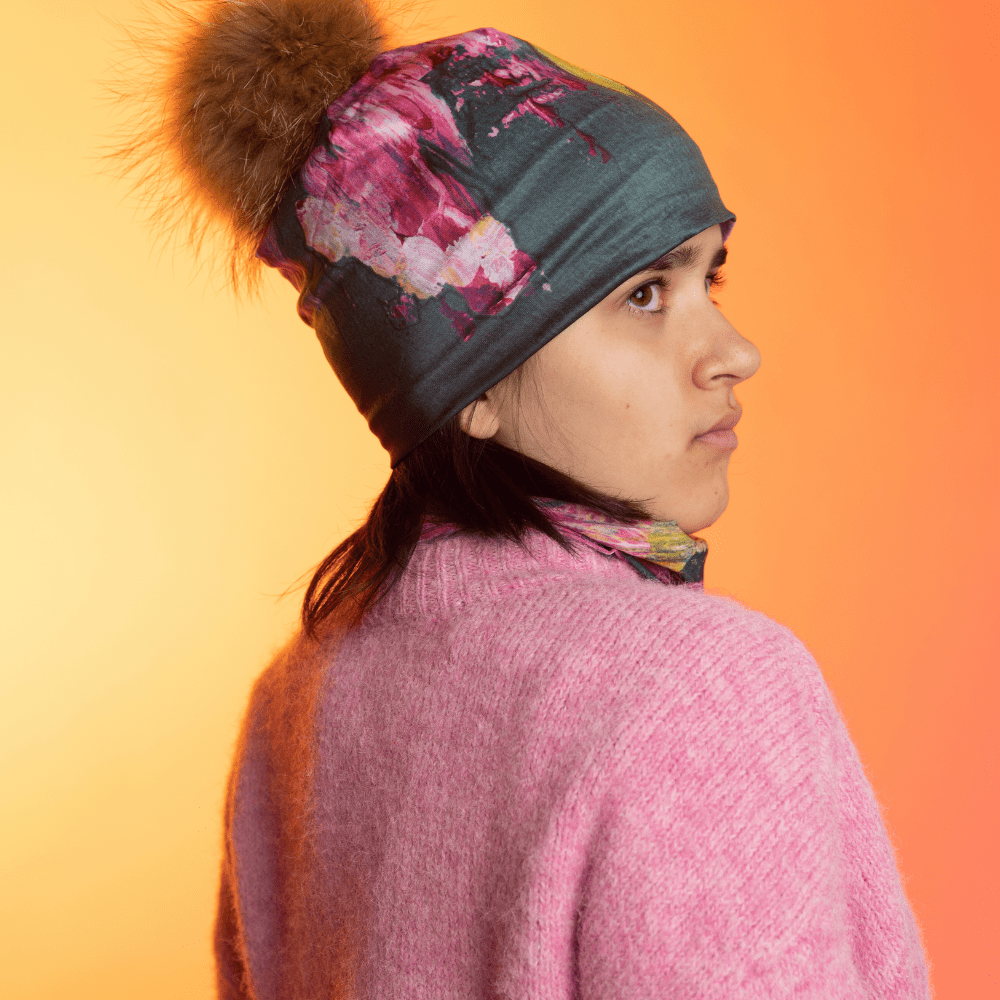 Une jeune personne portant la Tuque Fleur Glitch et une cache-cou assortie, vue de dos sur un fond à dégradé chaud.