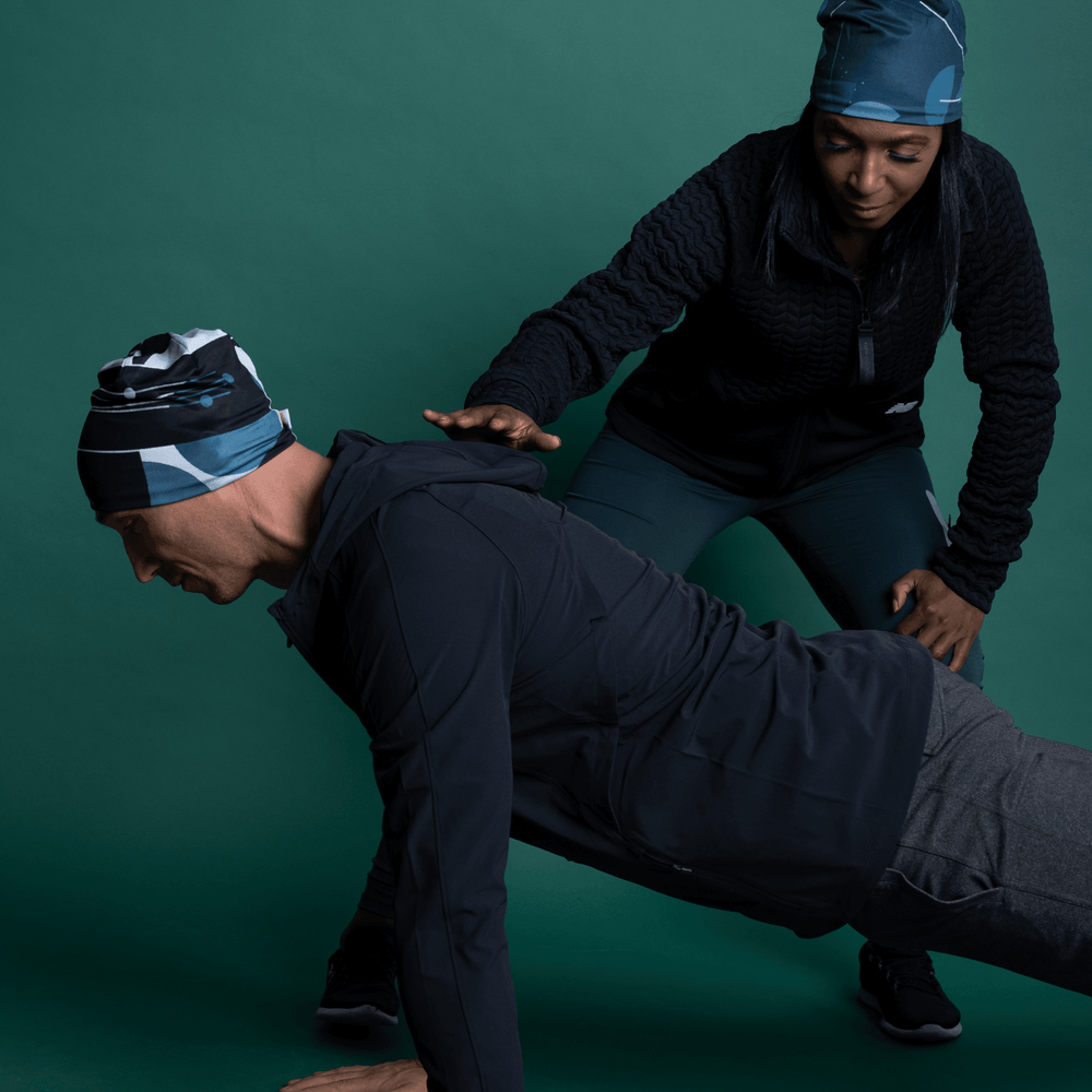 Un homme et une femme portant des tuques en extérieur; l'homme fait la planche tandis que la femme l'aide.
