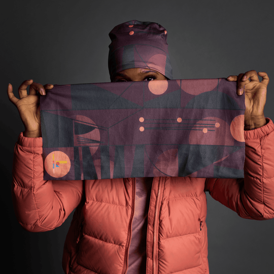 Une femme portant une veste matelassée corail tient un bandana déplié à motif géométrique violet.