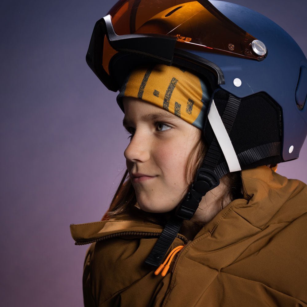 Young skier wearing the colourful orange movement beanie under a navy ski helmet with orange goggles, purple studio light