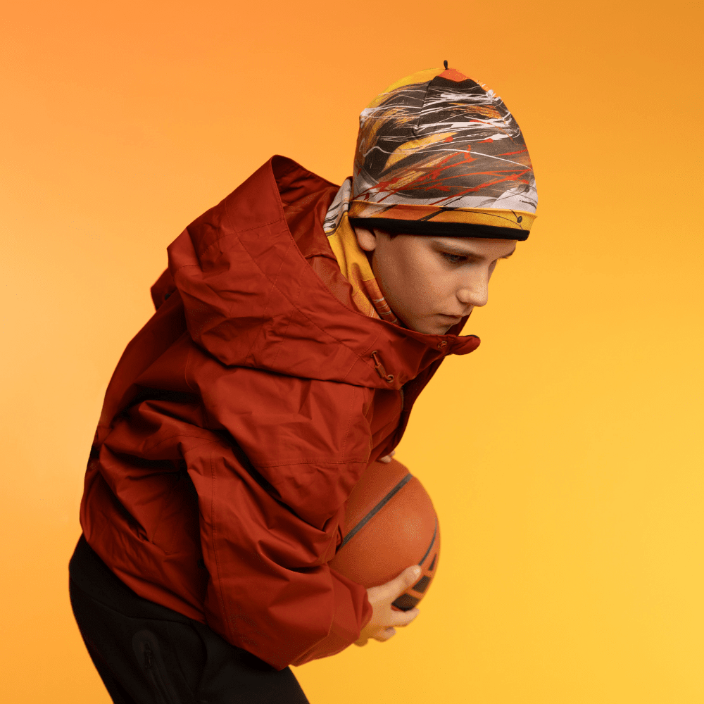 Jeune personne portant la tuque Le Cœur et une veste rouge, tenant un ballon de basket.