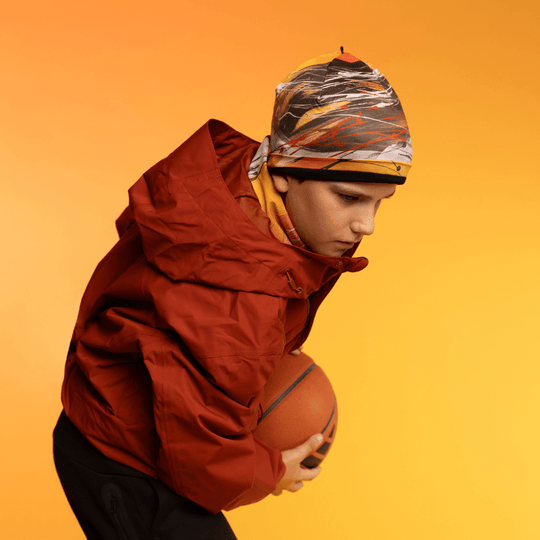 Jeune personne portant la tuque Le Cœur et une veste rouge, tenant un ballon de basket.