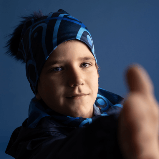 Un jeune garçon portant la tuque Bleu Mécanique et faisant un pouce levé, sur fond bleu.