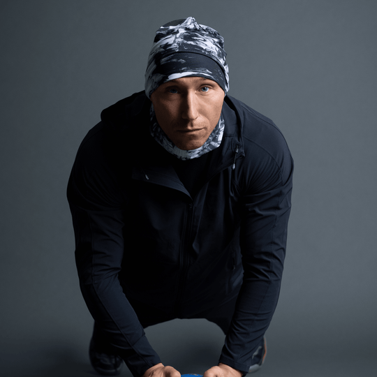 Homme en veste noire, portant une tuque et un cache-cou au motif abstrait noir et blanc, en pose pompe.