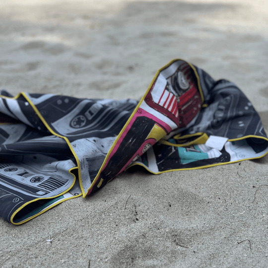 Gros plan de la serviette de plage Mixtapes pliée sur le sable, montrant le côté noir et blanc et le bord coloré.