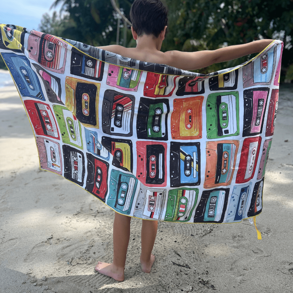 Enfant sur une plage tenant la face colorée de la serviette de plage réversible Mixtapes.