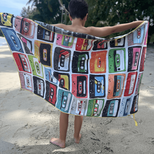 Enfant sur une plage tenant la face colorée de la serviette de plage réversible Mixtapes.