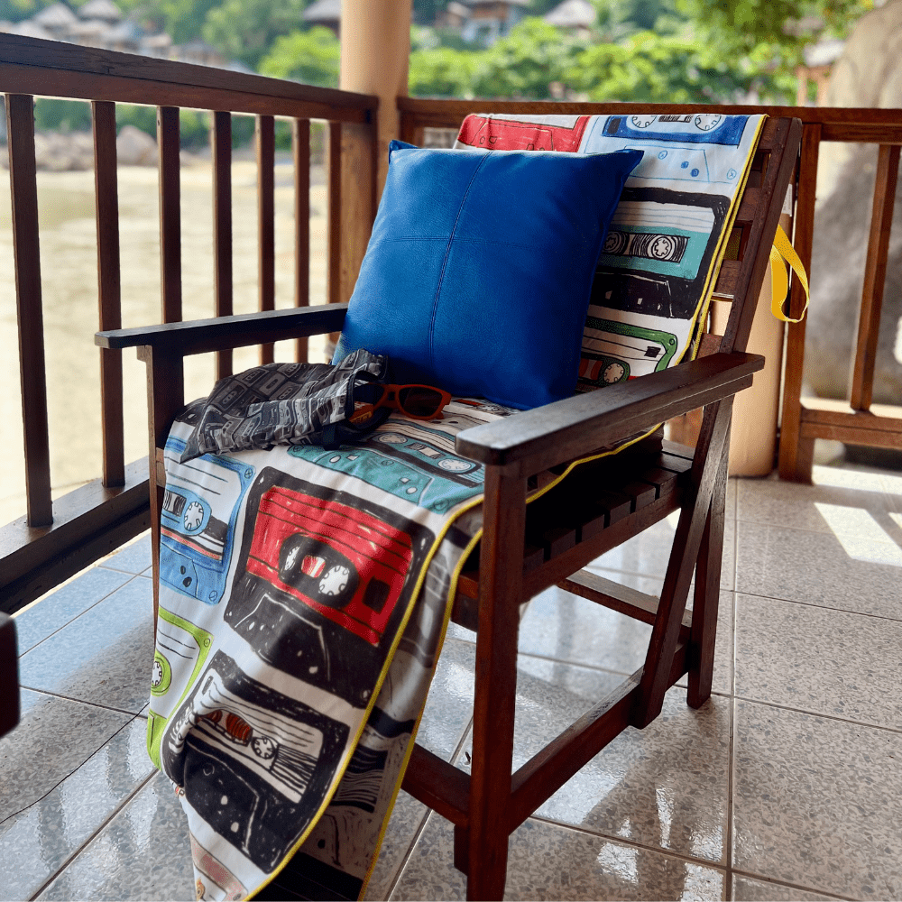Serviette de plage Mixtapes drapée sur une chaise en bois sur un balcon, à côté d&