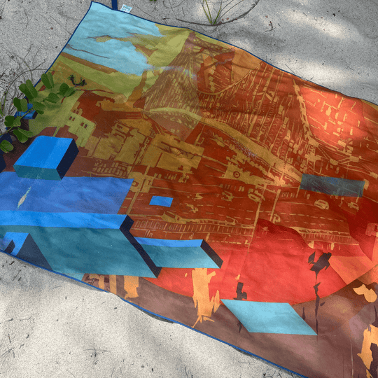 Serviette étalée sur le sable avec de la verdure, montrant le design artistique de style graffiti en entier.