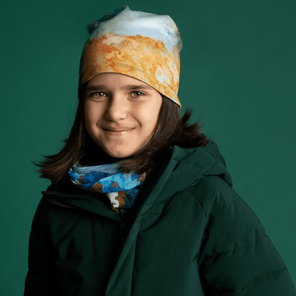 Une jeune fille portant la Tuque Marbre Océan et cache-cou assorti avec un manteau d'hiver vert foncé.
