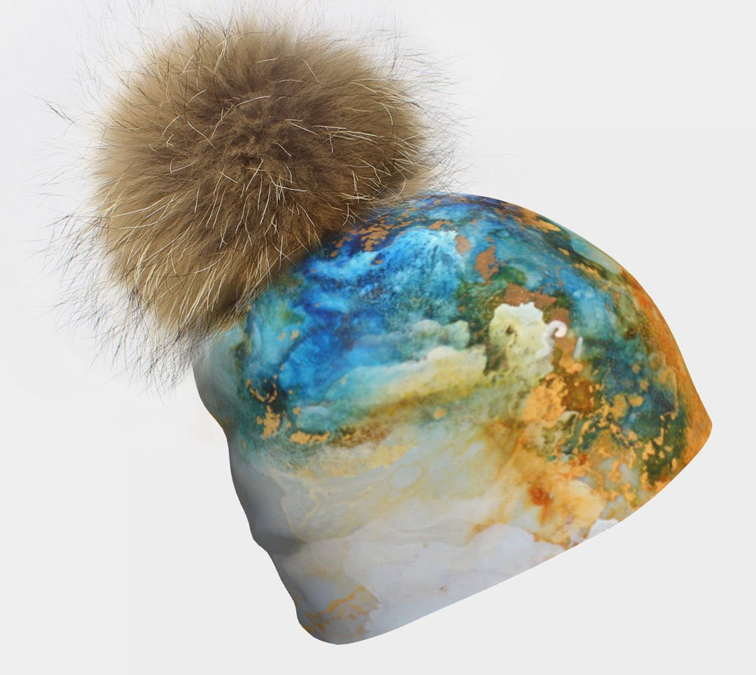 Gros plan d'une tuque à l'imprimé "Marbre Océan" coloré avec un gros pompon en fourrure naturelle moelleuse sur fond blanc.