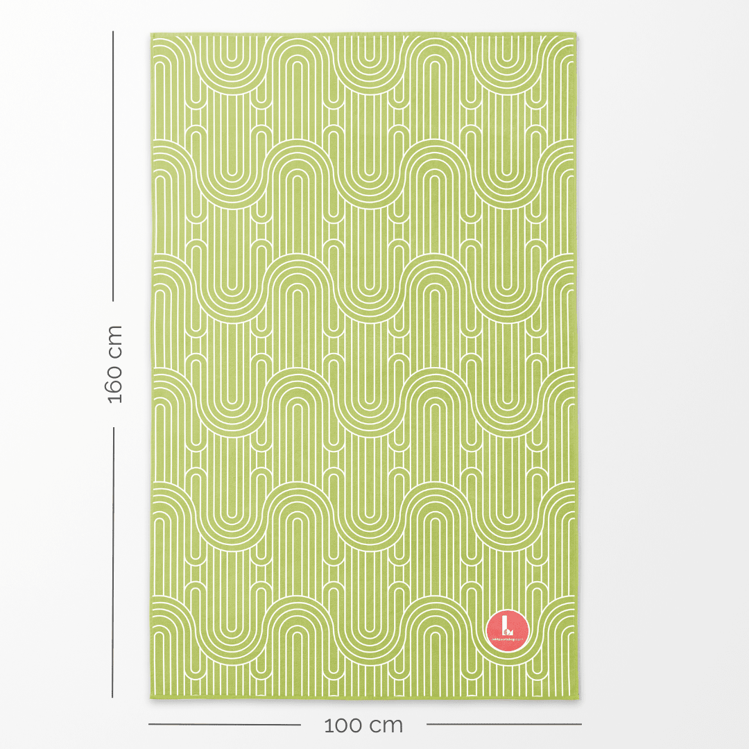 Une grande serviette en microfibre avec un motif géométrique vert exposée à plat avec indication des dimensions de 160 cm de longueur et 100 cm de largeur.