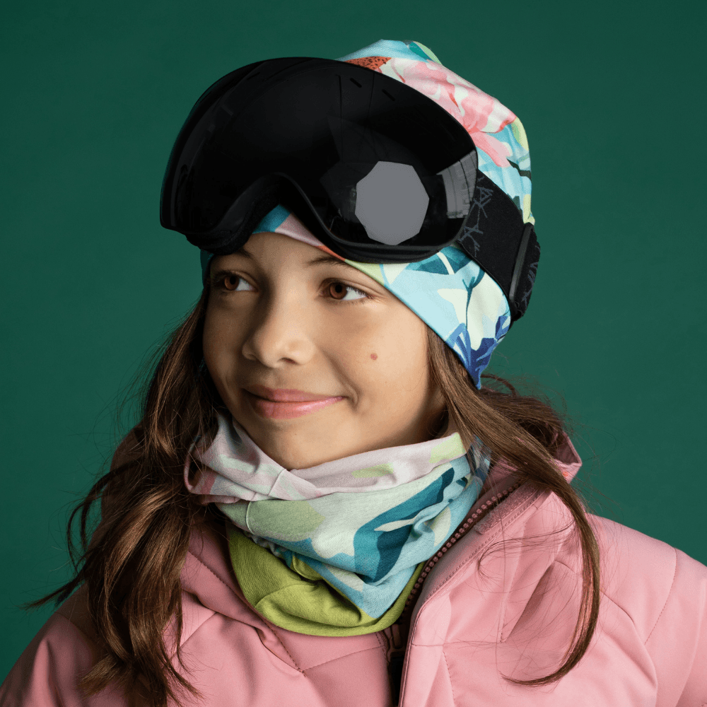 Une jeune fille portant une veste de ski rose et des lunettes, avec le cache-cou et la tuque assortis.