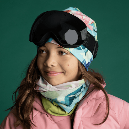 Une jeune fille portant une veste de ski rose et des lunettes, avec le cache-cou et la tuque assortis.