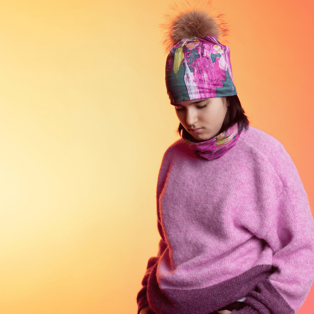 Une jeune personne portant un pull rose et une tuque et un cache-cou avec un art floral abstrait.