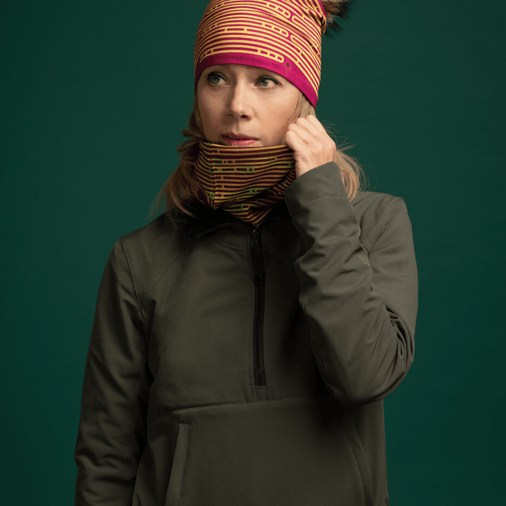 Femme portant une veste verte et un tube à motif, touchant le tissu près de son cou.