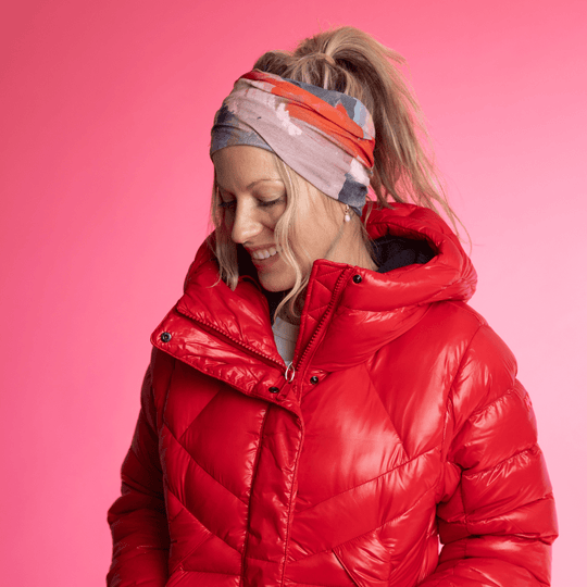 Femme portant le Tube Multifonction POLAR Rose &amp; Flammes en bandeau, regardant vers le bas avec un sourire, avec une veste d&