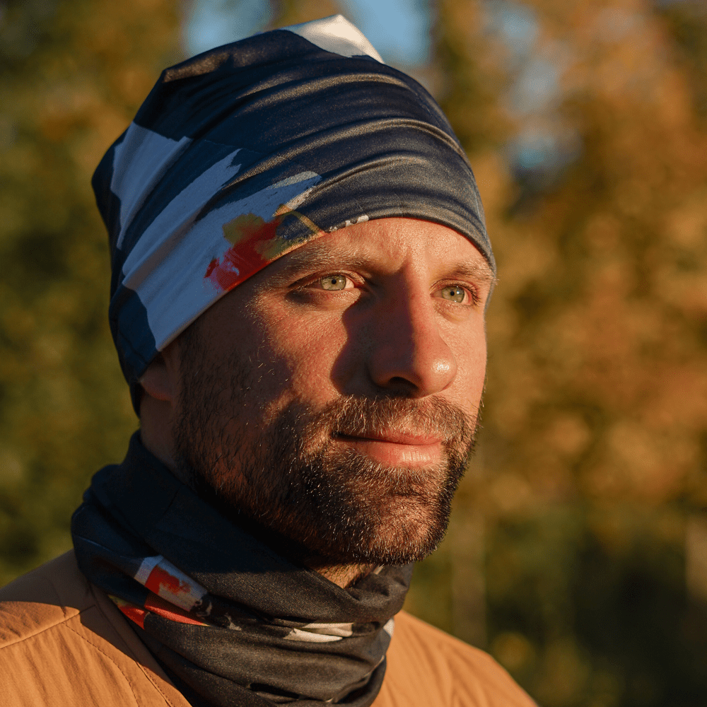 Man outdoors wearing a colorful abstract art patterned tube as a beanie and neck scarf.