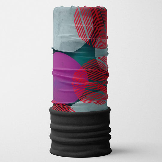 Un tube multifonctionnel POLAR Pois turquoise plié, montrant des motifs abstraits de pois turquoise, violets et rouges sur fond gris.