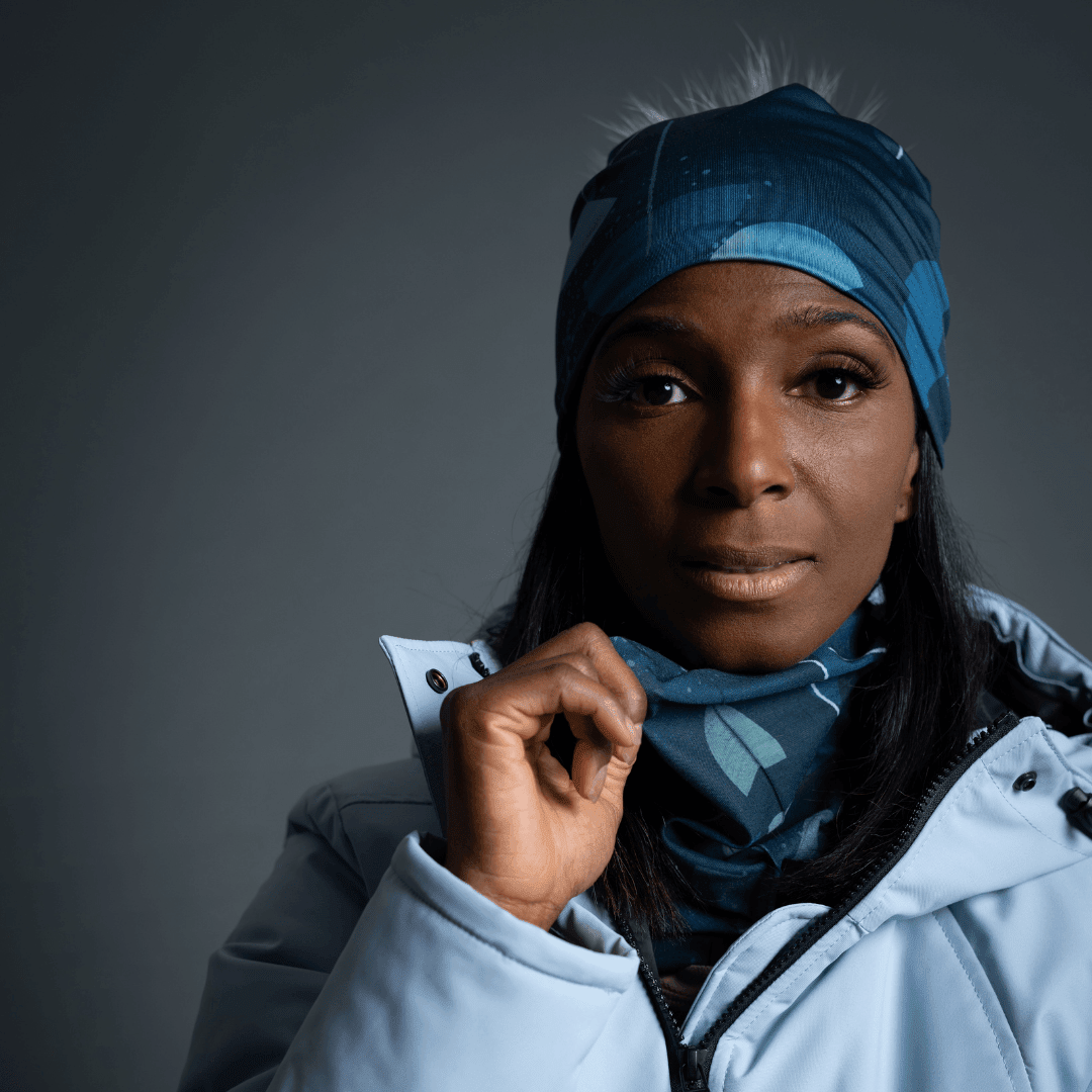 A woman wearing a light blue winter coat pulls the patterned POLAR Umbrella Teal neck tube higher around her neck, revealing the artistic design.