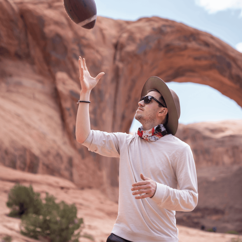 Un homme portant un bandana rouge et blanc autour du cou en lançant un ballon de football dehors.