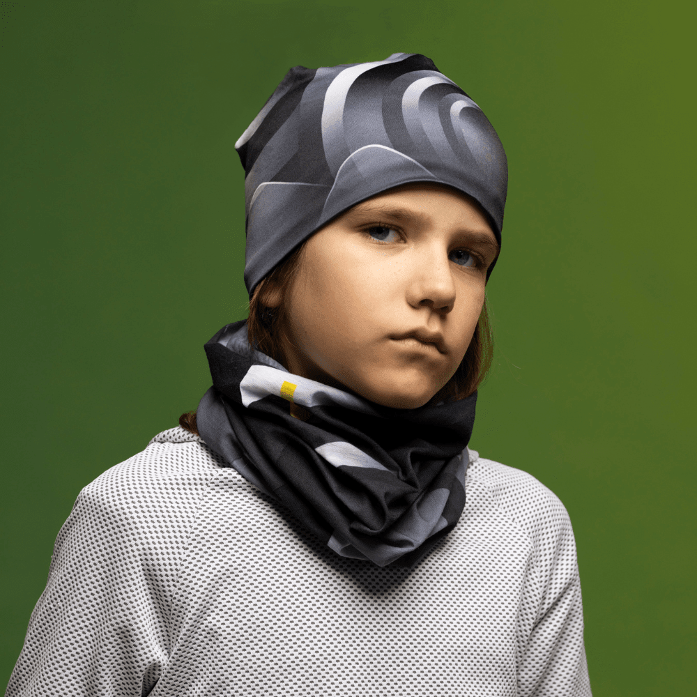 A young person wearing the beanie and a matching neck gaiter with a neutral expression, set against a green background.