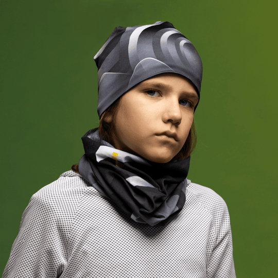 A young person wearing the beanie and a matching neck gaiter with a neutral expression, set against a green background.