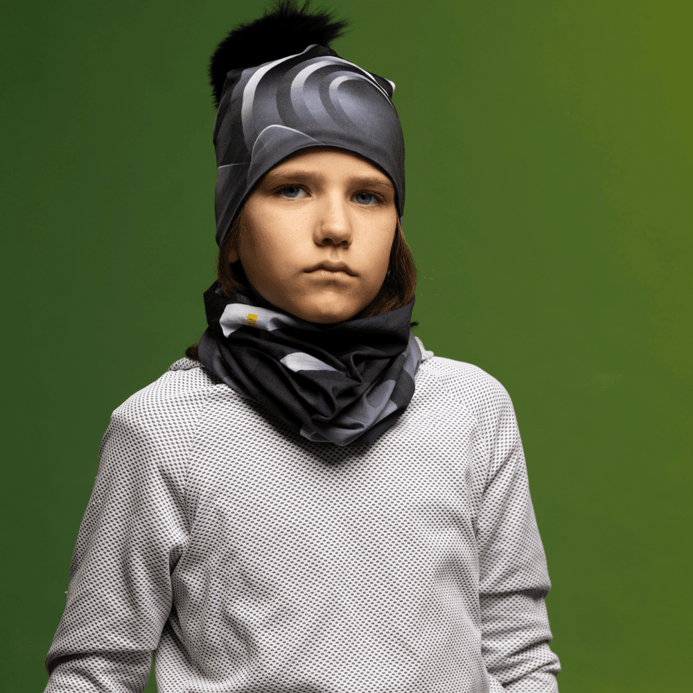 Enfant portant une tuque et un cache-cou avec un motif abstrait de vagues noires et grises.