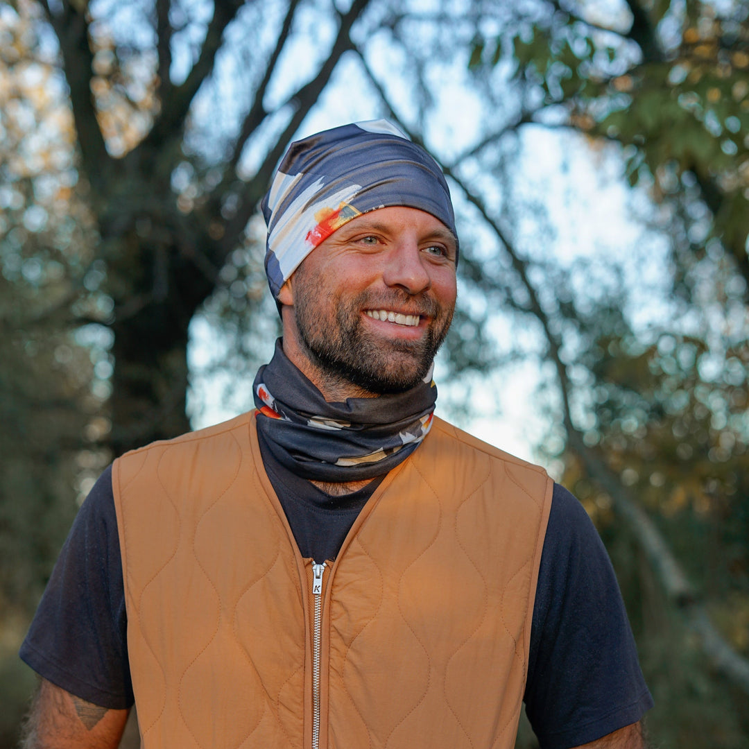 Man wearing a bandana tube as a headband and neck gaiter, smiling outdoors.