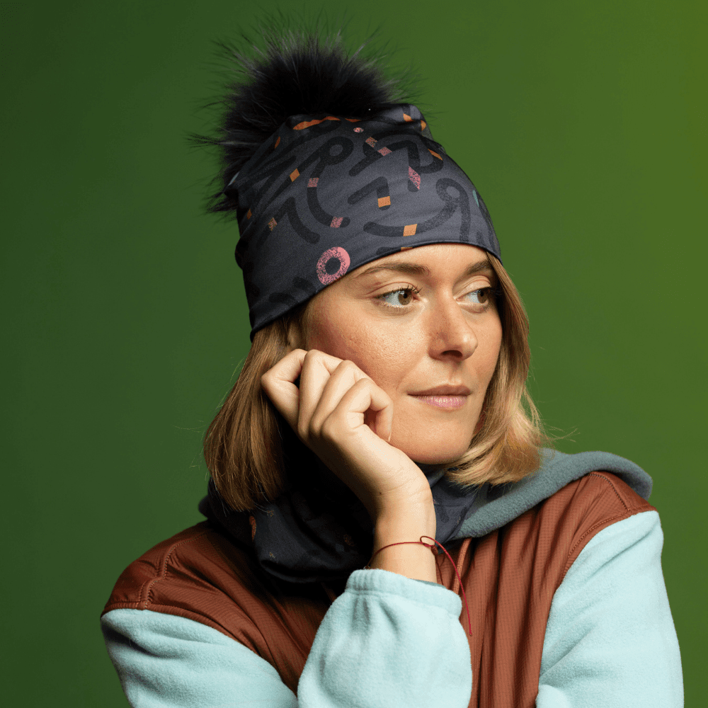 Femme portant une tuque grise avec pompon noir et cache-cou assorti, regardant sur le côté.
