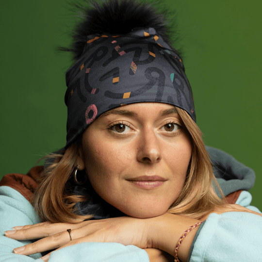 Femme portant une tuque grise avec pompon noir et cache-cou assorti, posant les mains jointes.