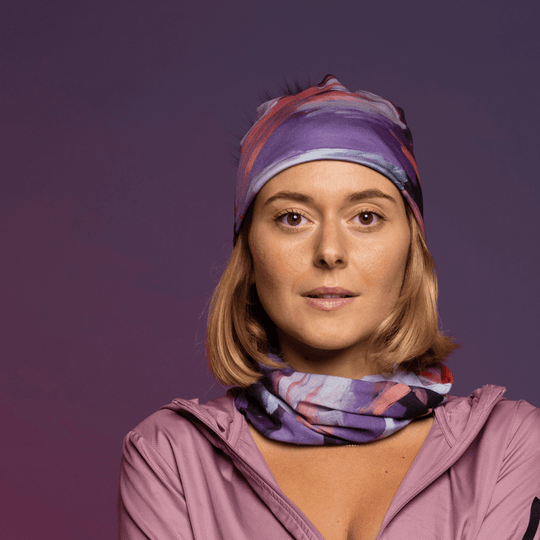 A woman wears a matching beanie and neck tube with a floral art print, posing against a purple background.