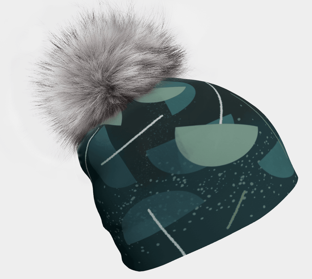 Gros plan d'une tuque bleu-vert foncé avec un motif abstrait bleu-vert et vert et un pompon gris moelleux.
