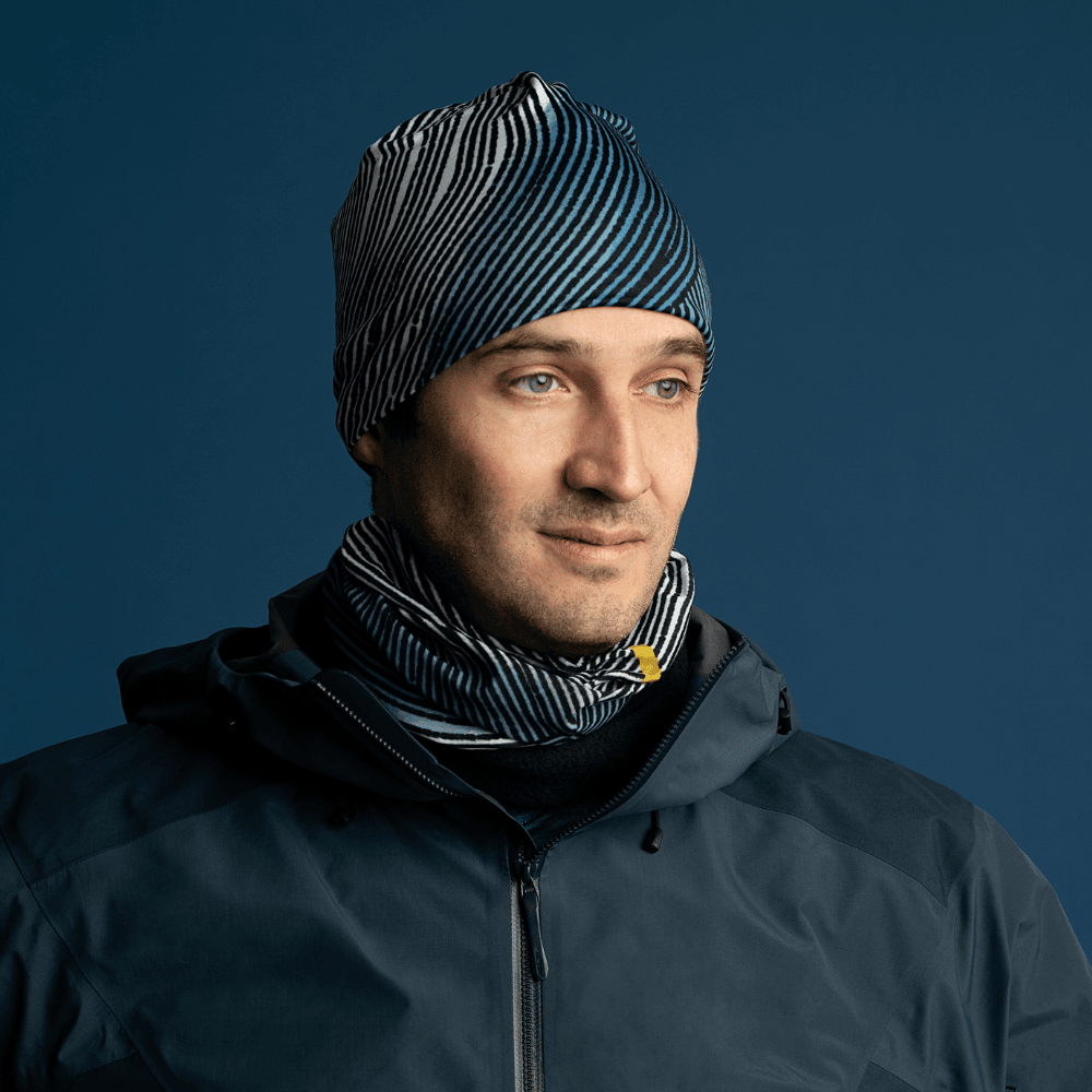 Un homme portant une veste noire, une cache-cou assortie à rayures abstraites et la tuque à rayures abstraites.