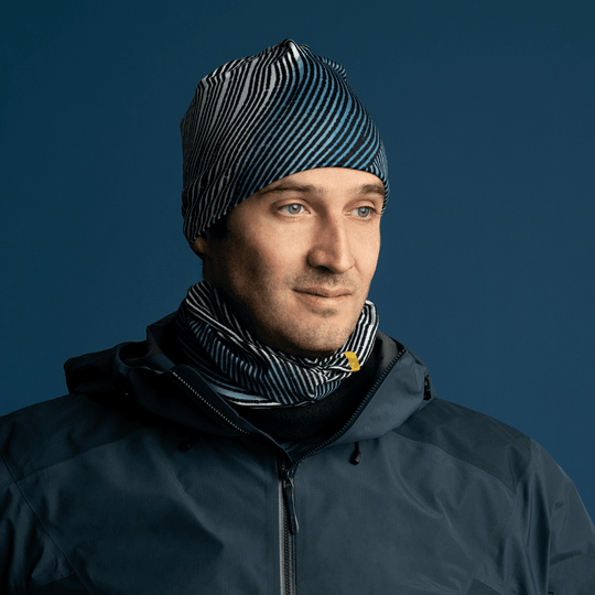 Un homme portant une veste noire, une cache-cou assortie à rayures abstraites et la tuque à rayures abstraites.