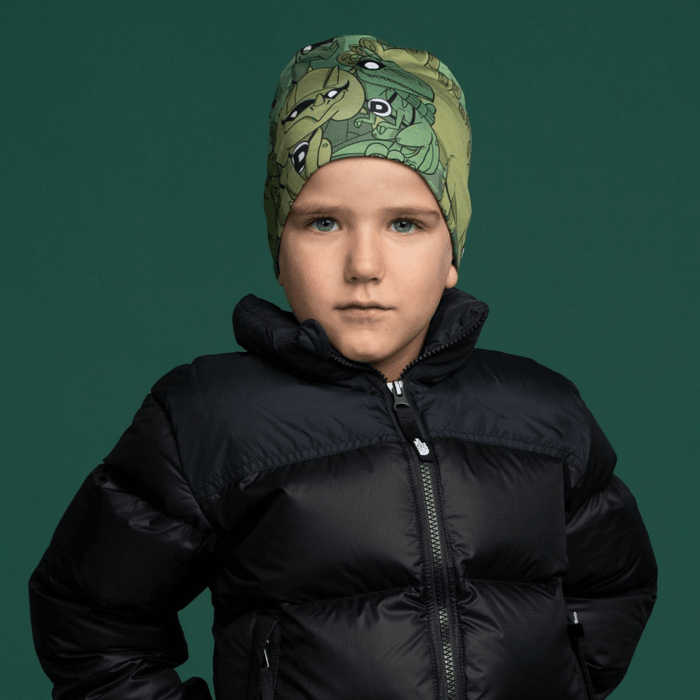 Un jeune garçon portant la tuque verte à thème de dinosaures et une veste noire.