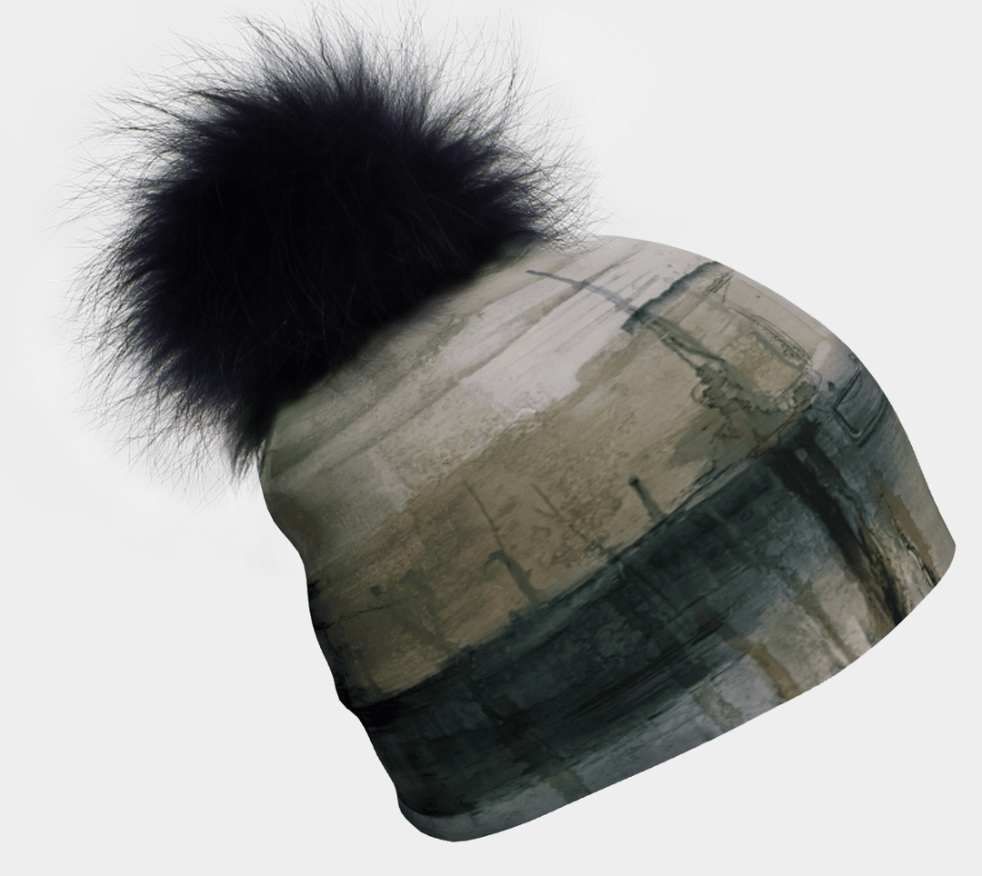 Une tuque abstraite verte et grise avec un grand pompon noir en fourrure est présentée sur fond blanc.